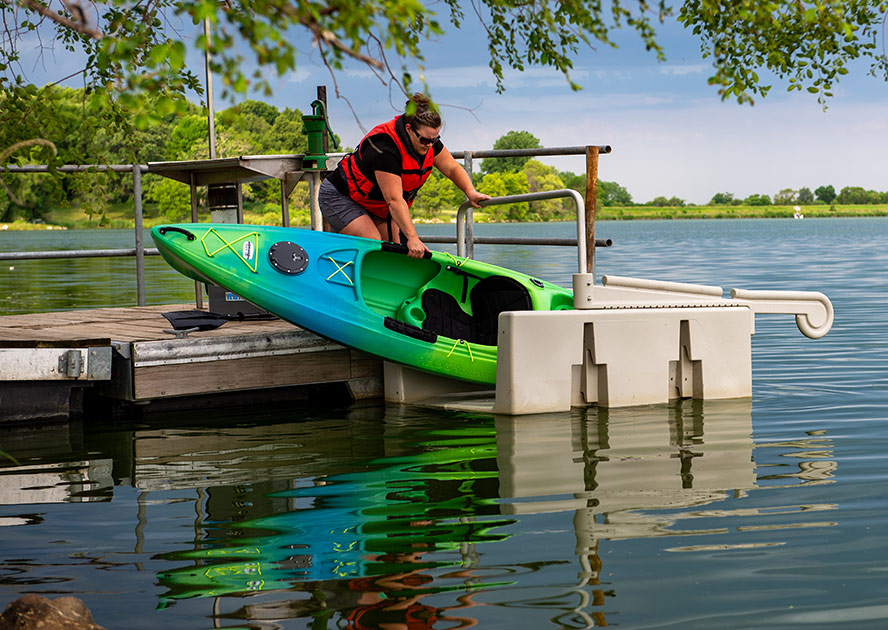 Person entering a kayak from a floating kayak launch, featuring a stable, slip-resistant platform with integrated handrails, designed for safe and easy water access.